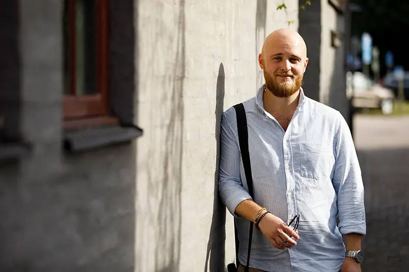 Mattias Svensson står lutad mot en husvägg. 