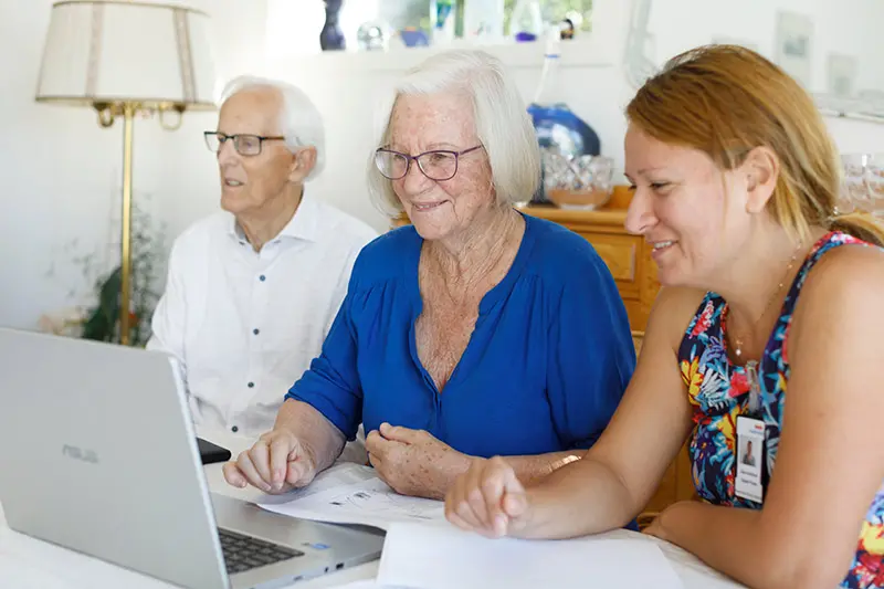 En kvinna sitter med ett äldre par vid en dator. 