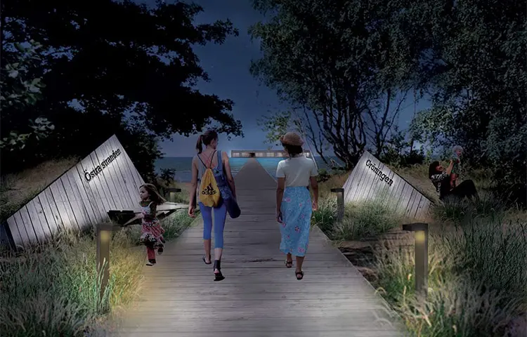 Två kvinnor går på en träspång mot havet. På varje sida finns en träskylt med texten "Gröningen". Det är kväll och lampor lyser upp spången. En brygga leder till ett kallbadhus.