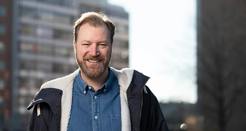 Porträtt av Johan Björnqvist. Han har kort hår, skägg och ler stort mot kameran.