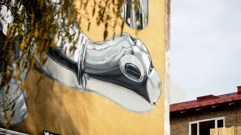 En målning på en husvägg i fotografisk stil. Motivet är en silverballong i form av en dinosaurie.