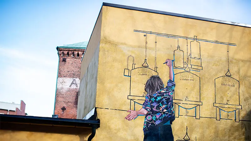 En väggmålning som föreställer ett barn bakifrån som ritar en teckning av apparater i ett bryggeri.