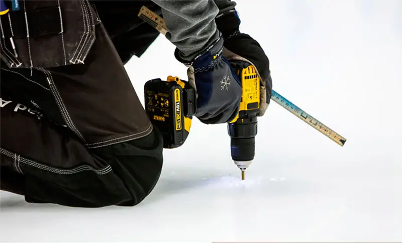En närbild på en handhållen borrmaskin som borrar ett hål i isen.