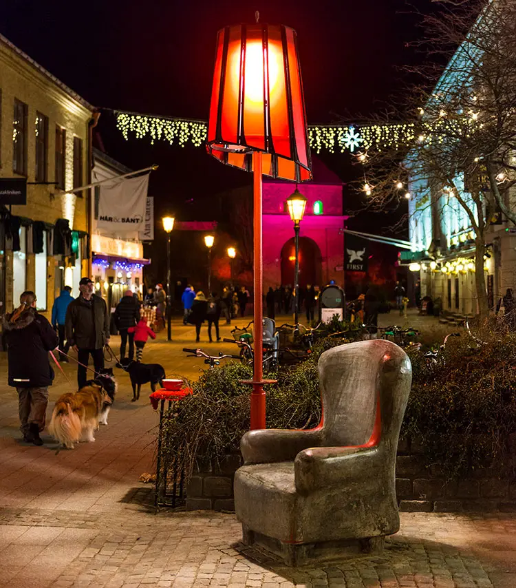 En fåtölj av betong står mitt på Storgatan. Bredvid finns en stor röd lampa. 