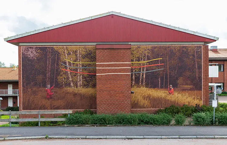 Målningen av en skogsglänta sträcker sig över hela husväggen. Den är delad i mitten, men hålls samman av två personer som håller en vimpel mellan sig.