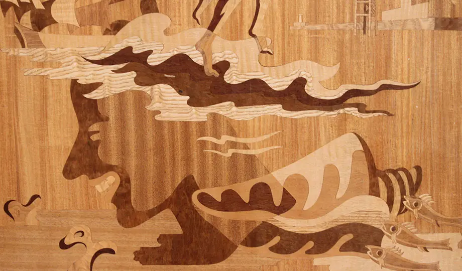 Del av ett verk där trä i olika färger bildar ett ansikte, vågor, snäcka och fiskar. 
