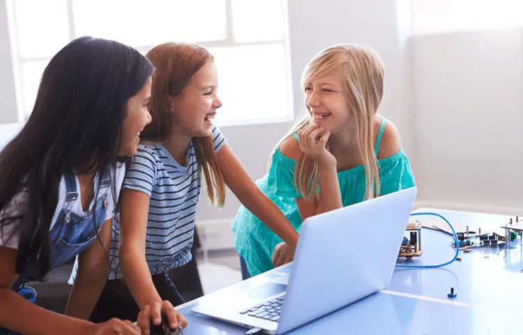 Tre barn sitter framför en dator och skrattar