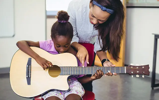 flicka med gitarr blir instruerad av lärare