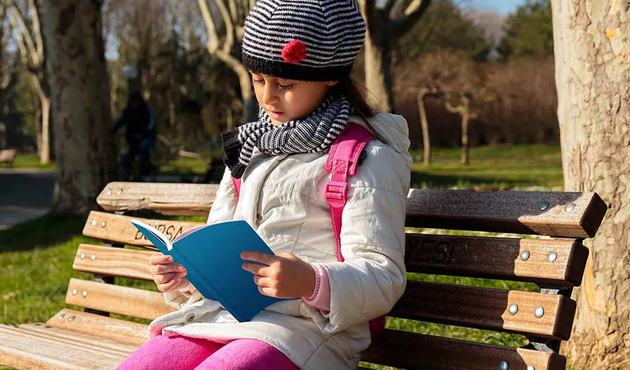 Flicka med ytterkläder sitter på parkbänk och läser