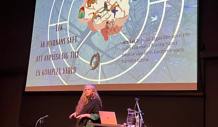 kvinna på scen med mikrofon, dator, framför stor visningsduk med text och en illustration av hjärnan