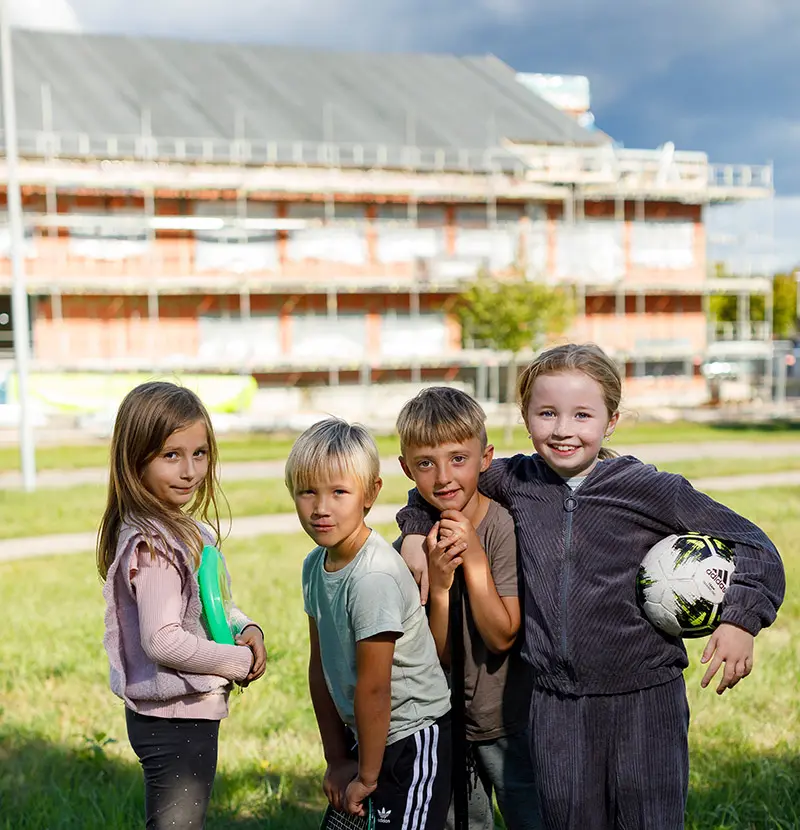 Fyra barn står framför en skola som håller på att byggas. 
