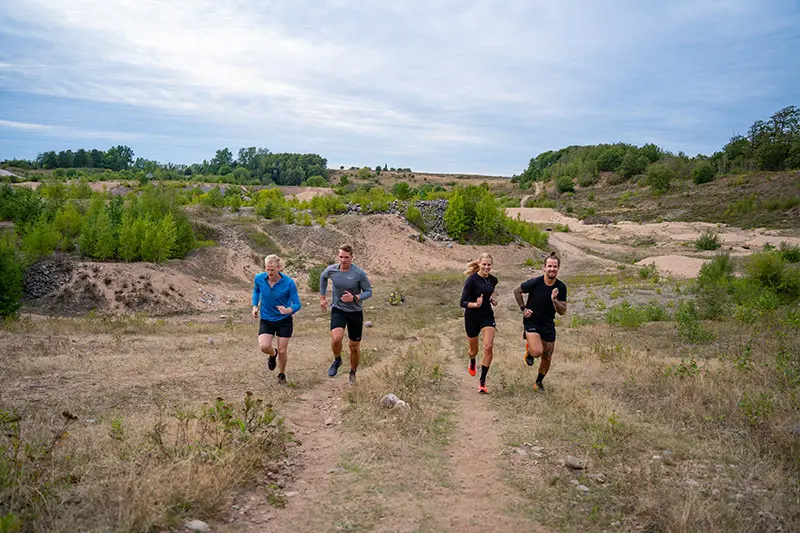 Fyra löpare springer uppför en kulle. I bakgrunden syns grustagets slänter.